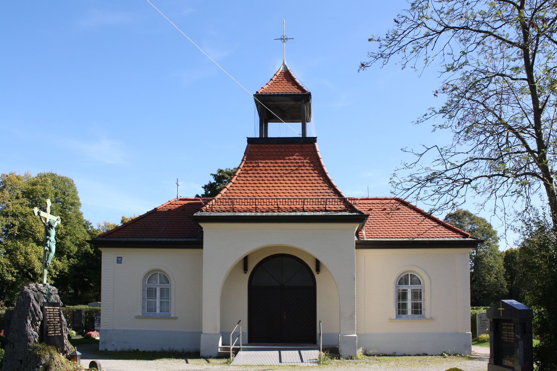 Front view of a small pale chapel with a red-tiled roof and bell turret at Riem Cemetery