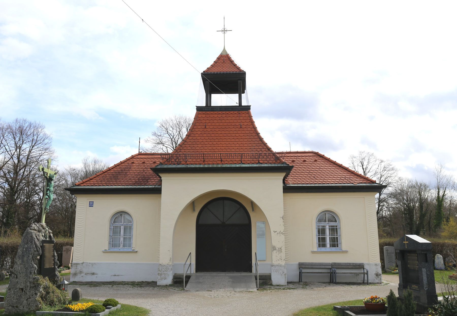 Small pale chapel with an arched portal, red-tiled roof and bell turret at Riem Cemetery